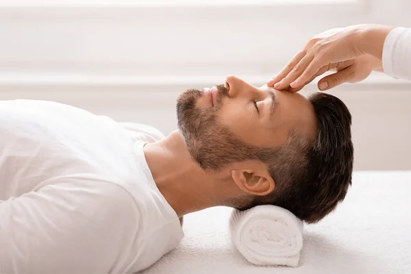 Masajista frotando relajado hombre frente, spa interior —  Fotos de Stock