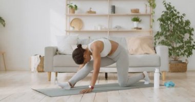Pilates eğitimi. Zarif afro-amerikan bayan kalçalarını ve bacaklarını yere uzatıyor, evde ayrılmaya hazırlanıyor.