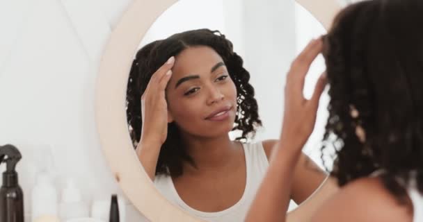 Giovane signora nera sana guardando specchio a casa, toccando il suo viso e godendo la sua condizione della pelle, rallentatore — Video Stock