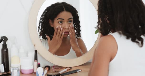 Zamartwiona młoda czarna kobieta patrząca w lustro, badająca zmarszczki w okolicach oczu, niezadowolona ze stanu skóry — Wideo stockowe