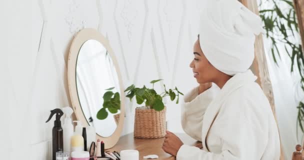 Retrato de mujer afroamericana atractiva feliz aplicando crema en la cara y sonriendo a la cámara, sentado en el baño — Vídeo de stock