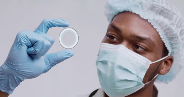 Африканский американский ученый в защитной маске и шляпе, держащий в руке голограмму с текстом Ковид-20, крупным планом — стоковое видео
