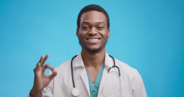 陽性のアフリカ系アメリカ人医師がOKサインと笑顔、青の背景をジェスチャー — ストック動画