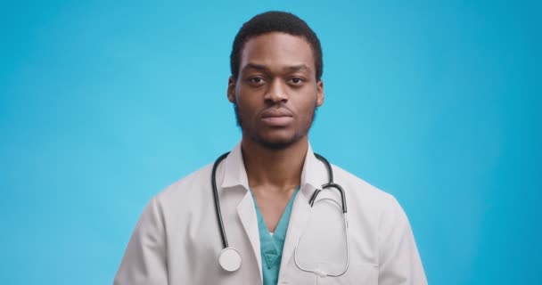 Retrato de estudio de médico negro grave cruzando las manos y sacudiendo la cabeza, expresando prohibición, fondo azul — Vídeos de Stock