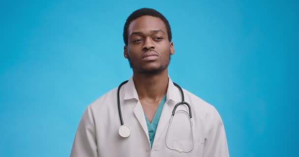 Médico afroamericano pensativo pensando en la situación epidémica, fondo de estudio azul — Vídeos de Stock