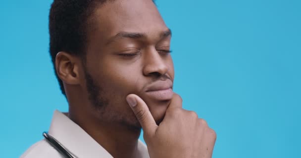 Dalgın Afrikalı Amerikalı genç bir doktorun portresi. Düşünceli yüz ifadeleri, mavi stüdyo geçmişi. — Stok video