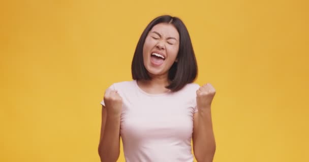 Äußerst glückliche junge Asiatin schreit laut, feiert ihren Erfolg und ihre Errungenschaften, orangefarbener Hintergrund — Stockvideo