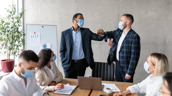 Dos hombres de negocios con máscaras golpeando codos durante la reunión corporativa interior — Foto de Stock
