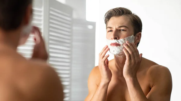 Confident young man looking in the mirror applying foam — Stock Photo, Image