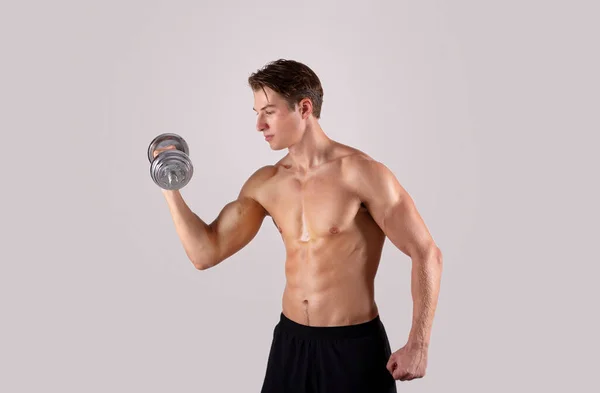 Bodybuilding strength workout. Young muscular man exercising with dumbbells, pumping up muscles on light background — Stock Photo, Image