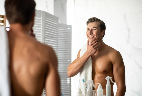 Selbstbewusster junger Mann blickt in den Spiegel, berührt Kinn — Stockfoto