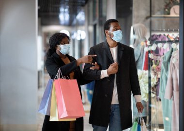Paketlerle alışveriş yaptıktan sonra milenyum Afro-Amerikan erkek ve kadın paltoları ve sağlık maskeleri.