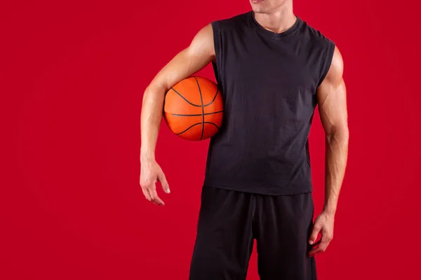 Vista cortada do jogador de basquete jovem segurando bola no fundo do estúdio vermelho, espaço de cópia — Fotografia de Stock