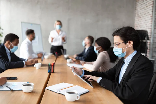 Asiatique homme d'affaires dans masque à l'aide de tablette pendant la réunion d'entreprise à l'intérieur — Photo