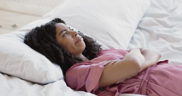 Ung irriterad afrikansk amerikansk kvinna liggande i sängen, irriterad av högljudda grannar, täcker öronen med händer — Stockvideo