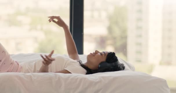 Boldog fekete nő zenét hallgat a fejhallgató, feküdt az ágyban, és tánc, oldalnézet — Stock videók