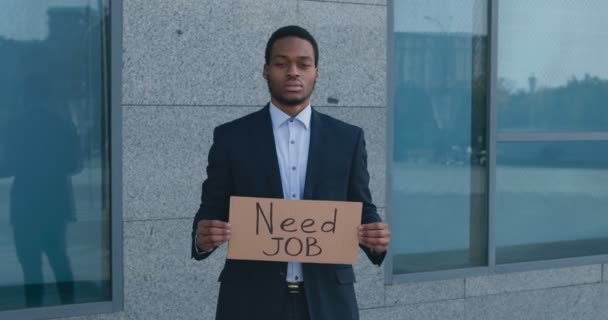 Retrato ao ar livre de jovem funcionário afro-americano de pé perto de prédio de escritórios com cartaz NECESSÁRIO JOB — Vídeo de Stock