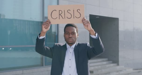 Коронакриз. Одинокий черный бизнесмен протестует возле бизнес-центра с плакатом CRISIS, отслеживая выстрел — стоковое видео