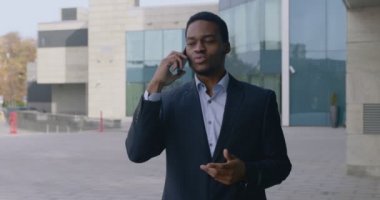 Duygusal Afrikalı Amerikalı iş adamı ortağıyla telefonda konuşuyor, sorunları çözüyor, iş alanında yürüyor.