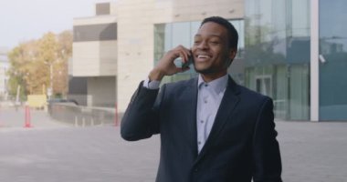 Yakışıklı zenci iş adamının açık hava portresi neşeli telefon konuşmaları, partnerlerle sohbet etmek ve gülümsemek.