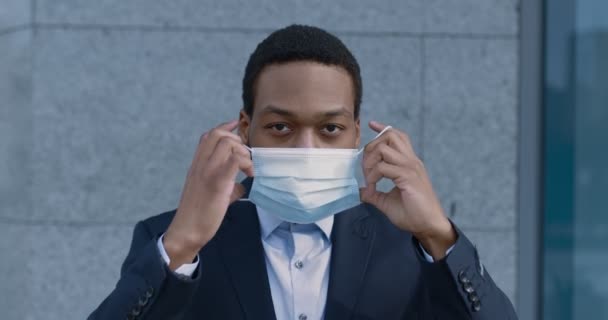 Zbliżenie portret poważnego amerykańskiego pracownika afrykańskiego zakładającego maskę ochronną, aby zapobiec zakażeniu koronawirusem — Wideo stockowe