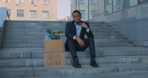 Black office manager sitting at business center with box of personal staff and placard Állást keres, nyomkövető lövés — Stock videók