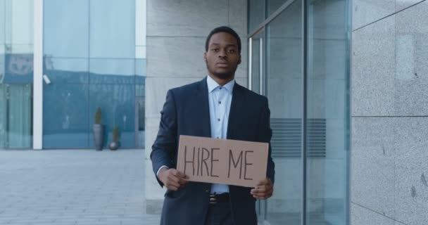 Θλιβερός Αφροαμερικάνος διευθυντής που ψάχνει για δουλειά, περπατώντας κοντά στο επιχειρηματικό κέντρο με αφίσα προσλάβετέ με, αργή κίνηση — Αρχείο Βίντεο