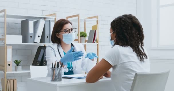 .Médica em máscara protetora consultando jovem paciente afro-americano durante consulta pessoal no hospital — Vídeo de Stock