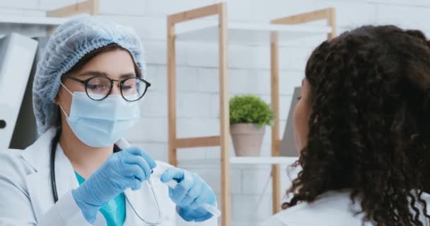 Orvos védő maszkban vesz pcr vizsgálati mintát fekete nő koronavírus tünetei — Stock videók