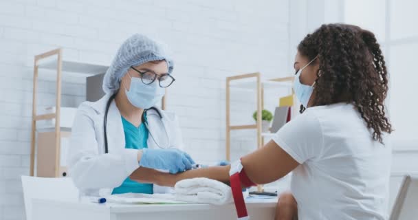 Лаборант в защитной маске делает внутривенное введение вакцины чёрной женщине в клинике — стоковое видео