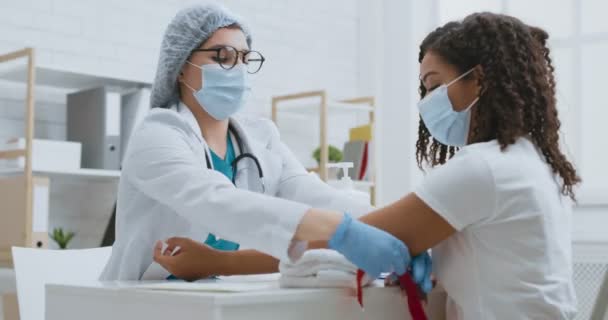 Asistente de laboratorio femenina que aplica torniquete en el brazo del paciente antes de tomar sangre venosa para análisis o inyección intravenosa — Vídeo de stock