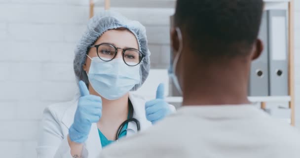 Mujer doctora hablando con paciente masculino durante cita personal durante pandemia de coronavirus, ambos en máscaras protectoras — Vídeo de stock