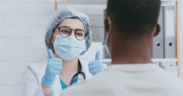 Mujer doctora hablando con paciente masculino durante cita personal durante pandemia de coronavirus, ambos en máscaras protectoras — Vídeos de Stock