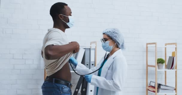 Gezondheidsonderzoek. Medische dokter luistert naar zwarte man borst, longen controleren met stethoscoop — Stockvideo