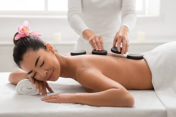 Розслаблена азіатська жінка насолоджується масажем гарячих каменів назад у спа-салоні — стокове фото