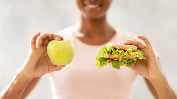 Konzept von gesundem versus Junk Food. Ausgeschnittene Ansicht der schwarzen Dame, die zwischen Cheeseburger und Apfel auf hellem Hintergrund wählen kann — Stockfoto
