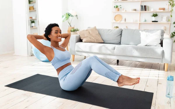 Полнометражный портрет молодой черной женщины, занимающейся на спортивном коврике, тренирующей мышцы дома — стоковое фото