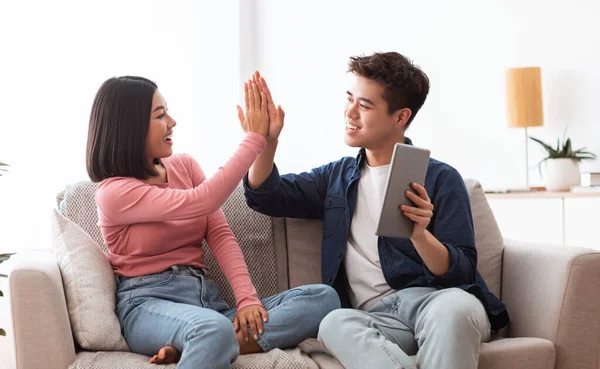 Casal asiático com tablet digital dando alta cinco sentado em casa — Fotografia de Stock