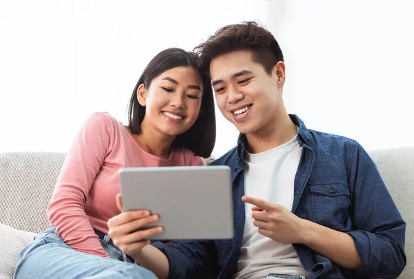 Asijské manžel a manželka pomocí tablet sedí na pohovce vnitřní — Stock fotografie