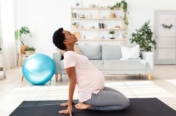 Vista lateral de una mujer embarazada negra haciendo backbend durante la meditación o yoga en casa — Foto de Stock