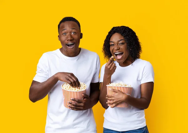 Laughing black man and woman eating popcorn on yellow background