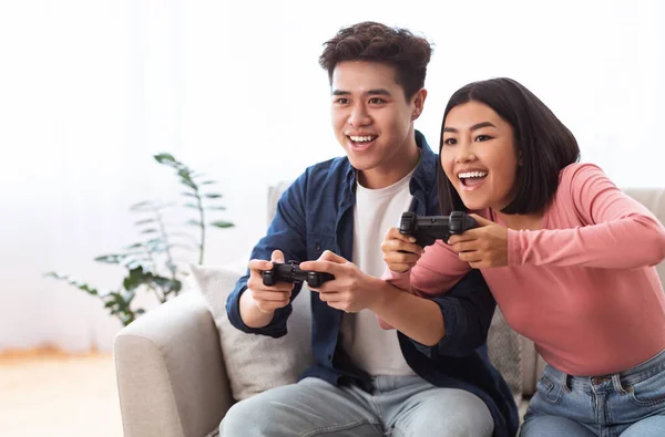 Emocionada pareja asiática jugando videojuegos sentada en el sofá en casa —  Fotos de Stock