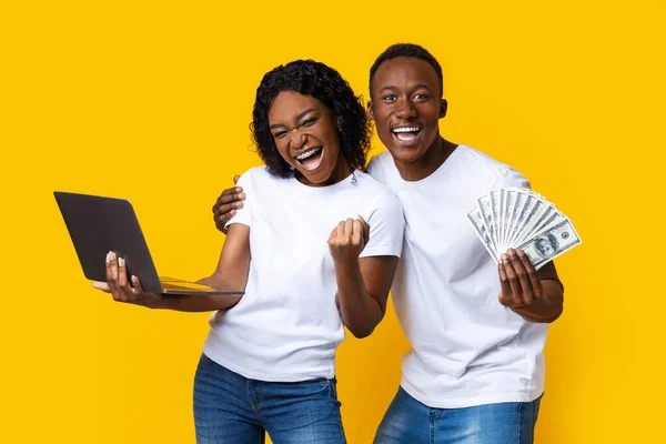 Feliz pareja negra celebrando ganar con el ordenador portátil y dinero en efectivo —  Fotos de Stock