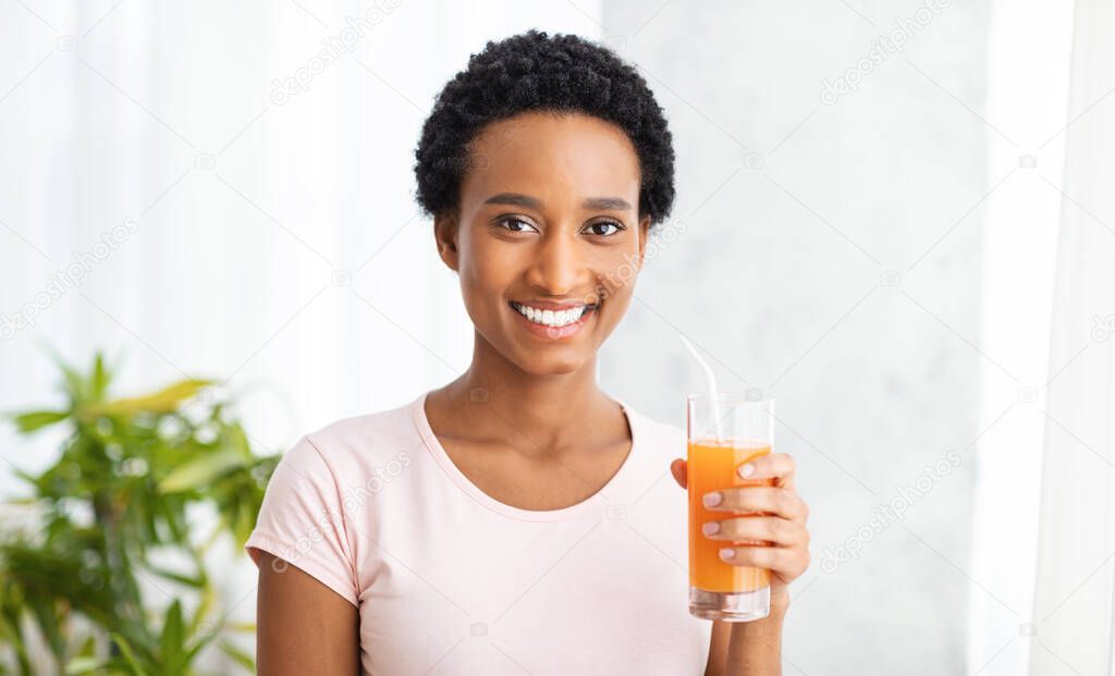 Healthy eating and detox concept. Smiling black woman with glass of fresh orange juice at home, panorama