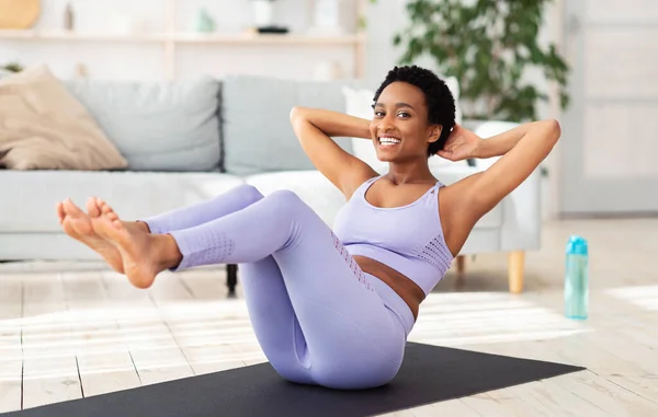 Sport podczas kwarantanny. Atrakcyjny czarny kobieta robi fitness na macie sportowej w domu, ćwiczy mięśnie brzucha — Zdjęcie stockowe