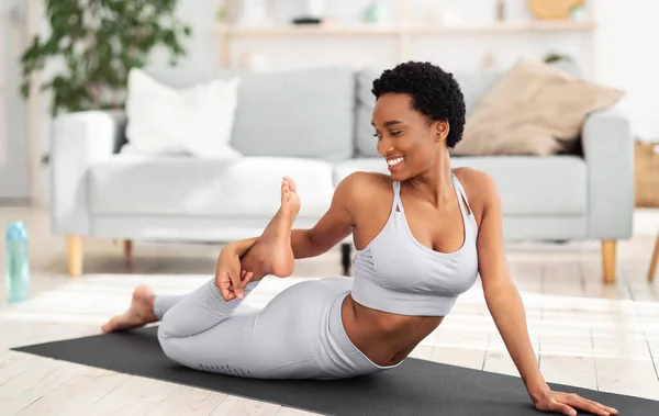 Heimisches Sportkonzept. Sportliche junge schwarze Frau in Sportbekleidung macht Fitnessübungen auf Yogamatte drinnen — Stockfoto