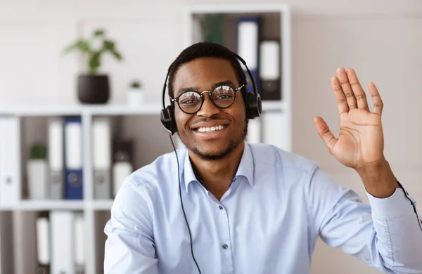 Glad sort konsulent med headset vinker på kameraet - Stock-foto