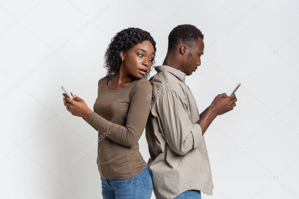 Black couple standing back to back, using smartphones
