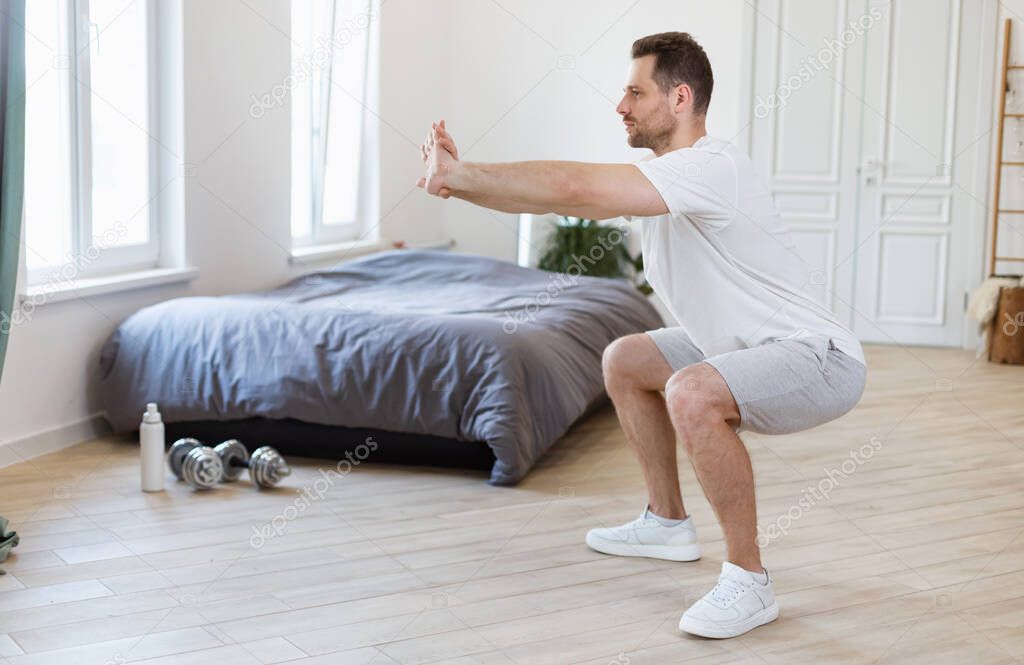 Sporty Guy Doing Two-Legged Squat Exercise At Home