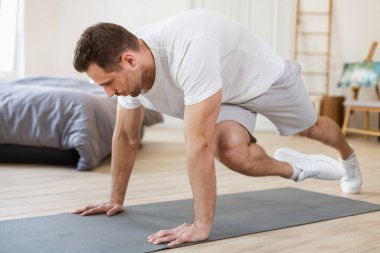 Egzersiz yapan adam yatak odasındaki zeminde koşu tahtası egzersizi yapıyor.